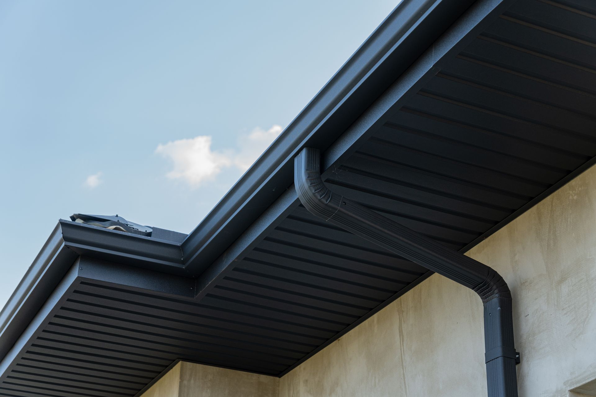 Dark charcoal gutters and soffits installed on the exterior of a light-colored building under a clear blue sky.