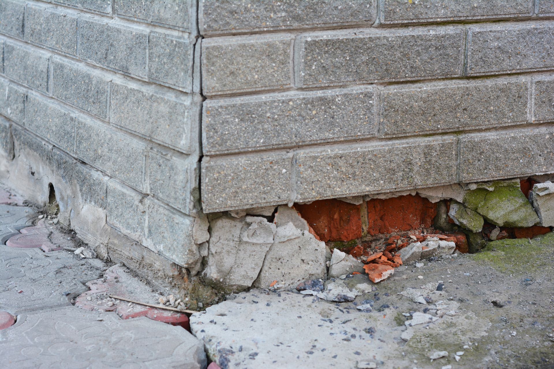 A close-up view of a building's exterior corner showing crumbled mortar, exposed red bricks, and a vertical wall crack.
