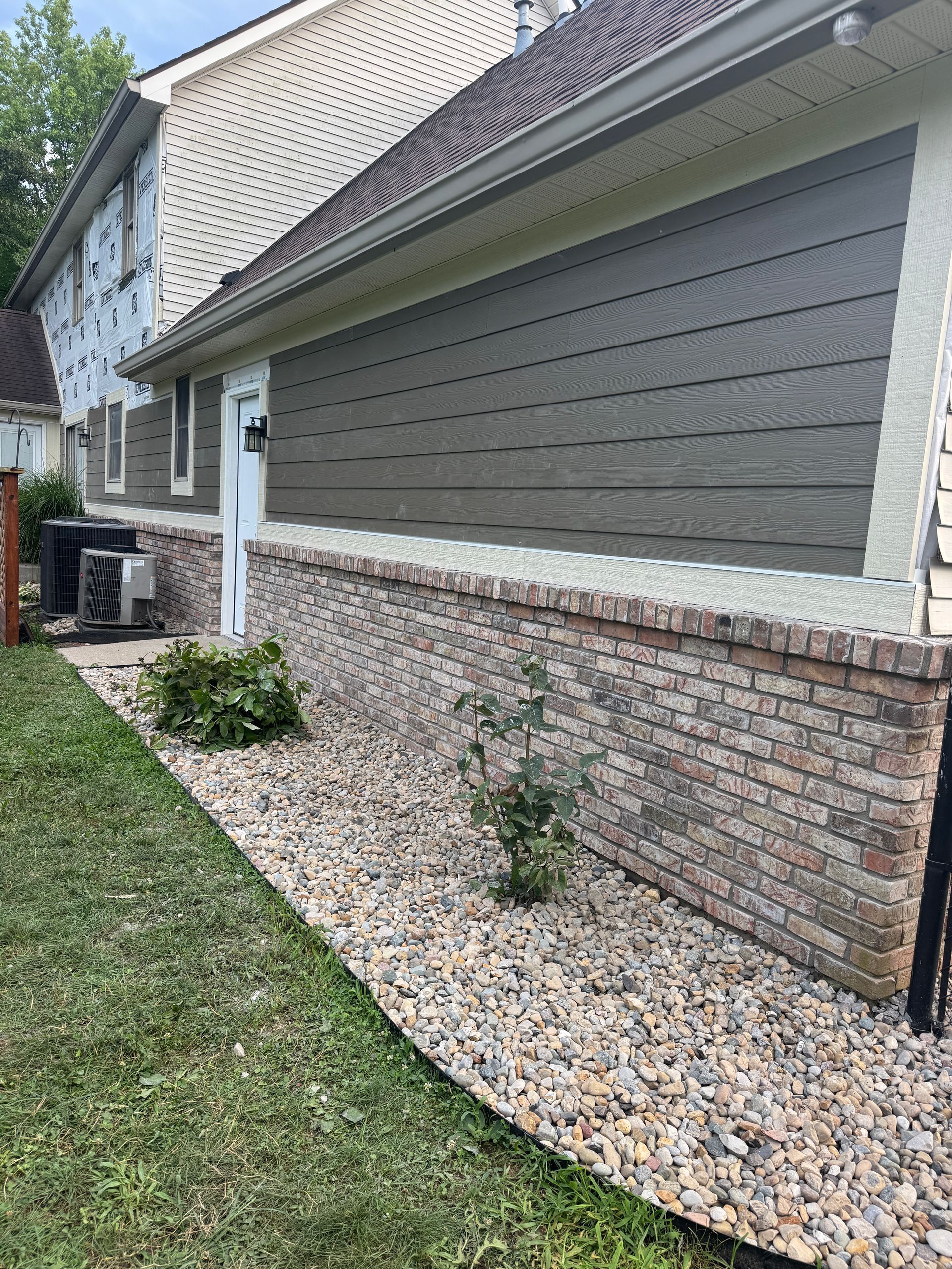 House exterior with gray siding, brick foundation, and a gravel bed along the wall