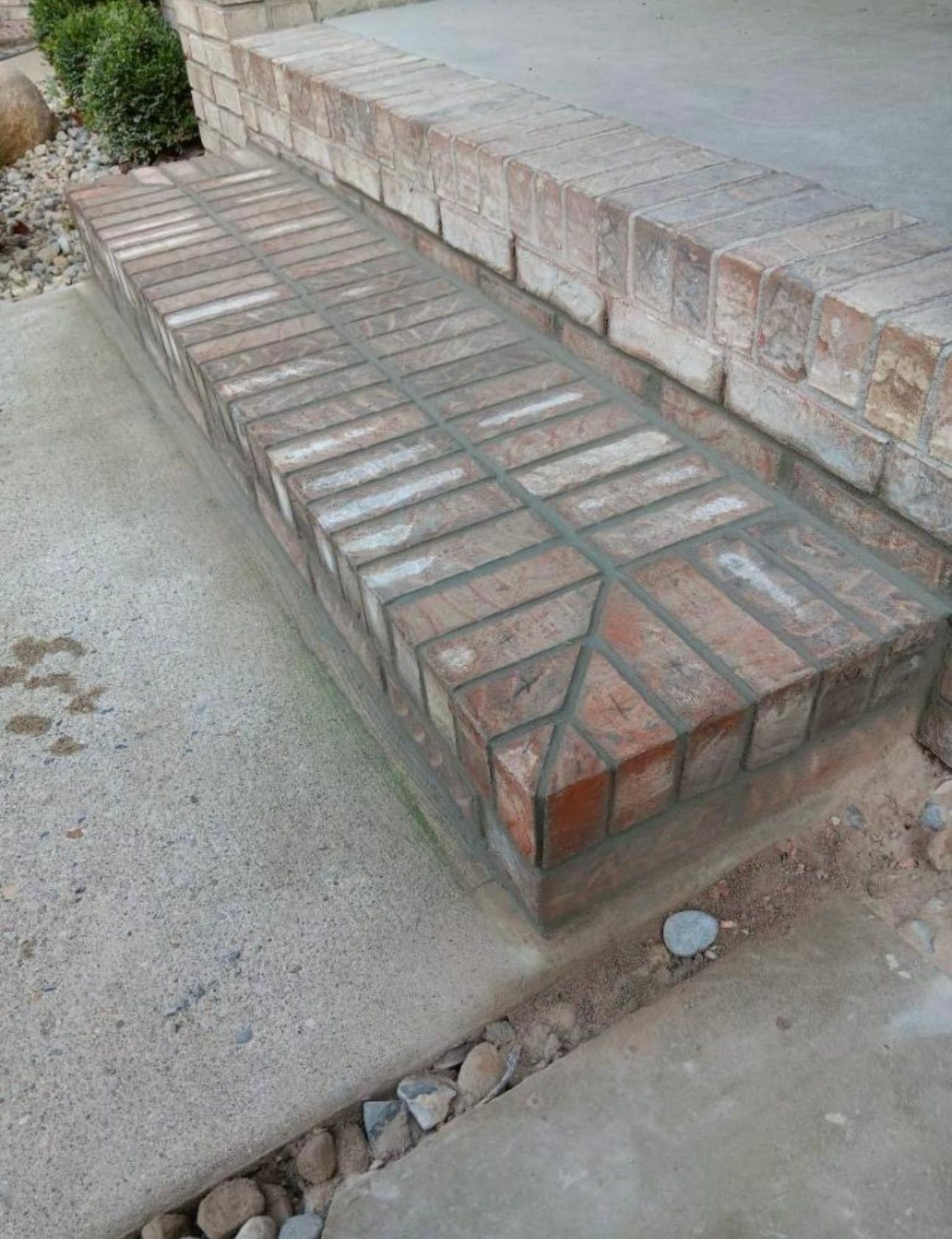 A single, rectangular brick step with a decorative herringbone pattern, leading up to a concrete porch.