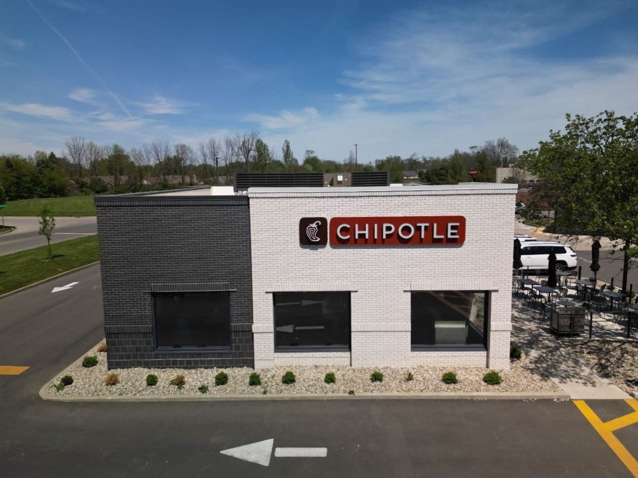 Chipotle restaurant exterior with white and gray facade, parking lot, and blue sky