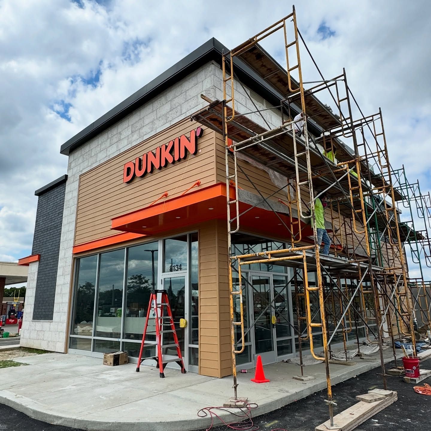 Dunkin’ storefront under construction with scaffolding, orange awning, and ladder outside
