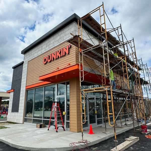 Dunkin’ storefront under construction with scaffolding, ladders, and orange awning
