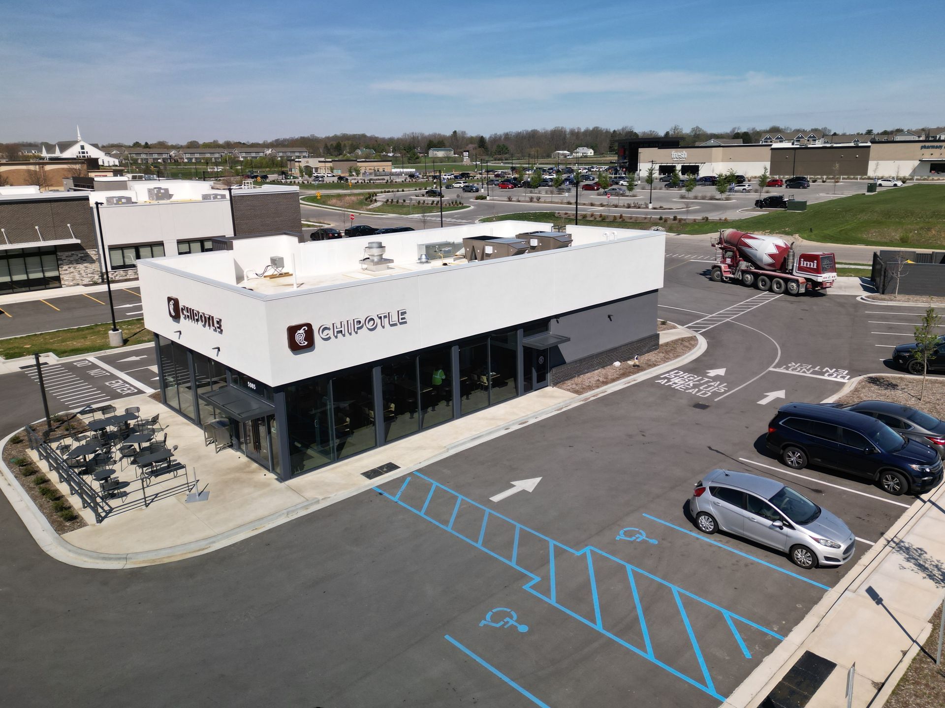 Aerial view of a white commercial building with a parking lot, blue accessible spaces, and a few parked cars.