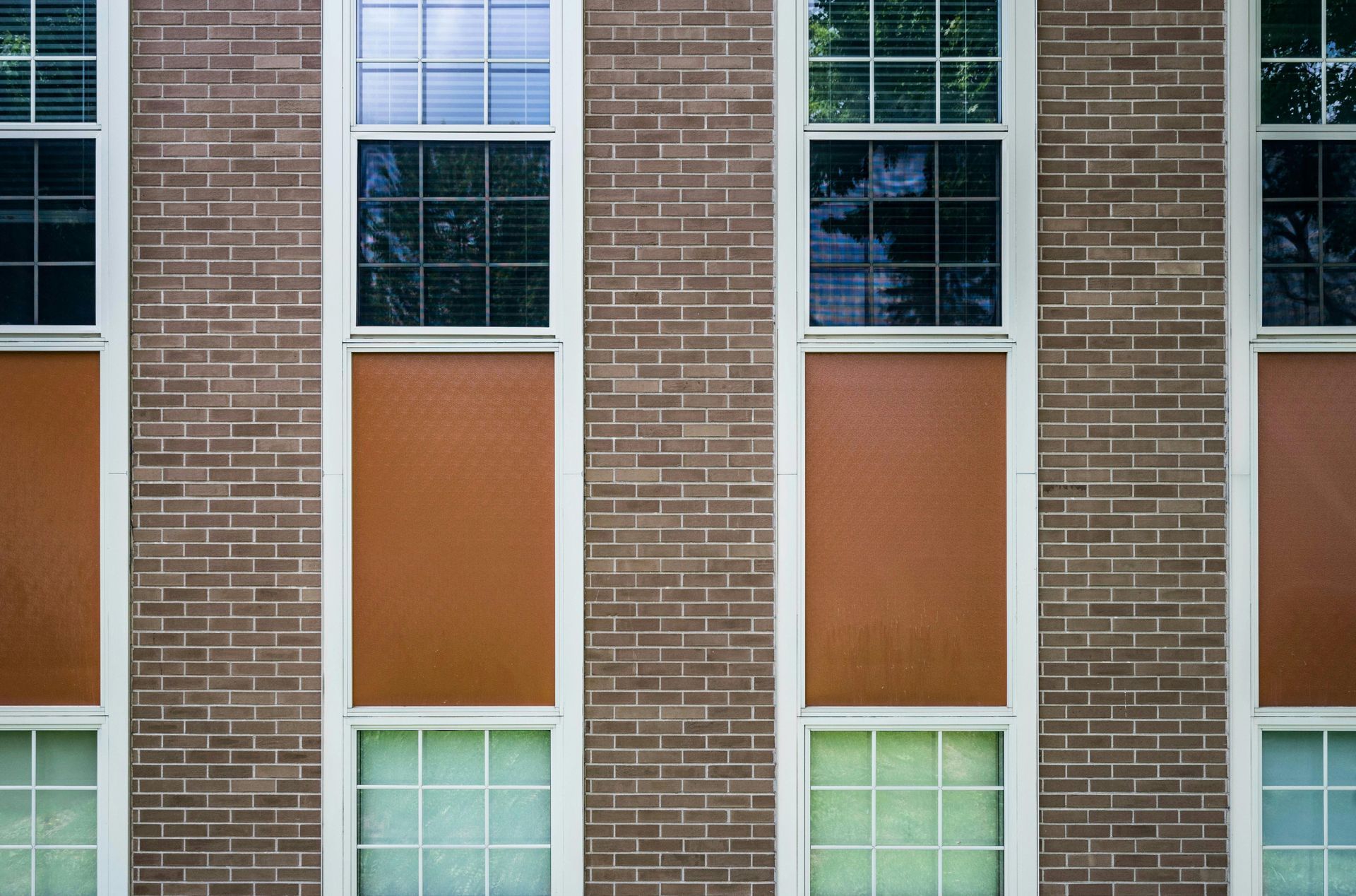 A brick wall with four vertical rows of windows, each alternating between glass panes and solid, orange-brown panels.