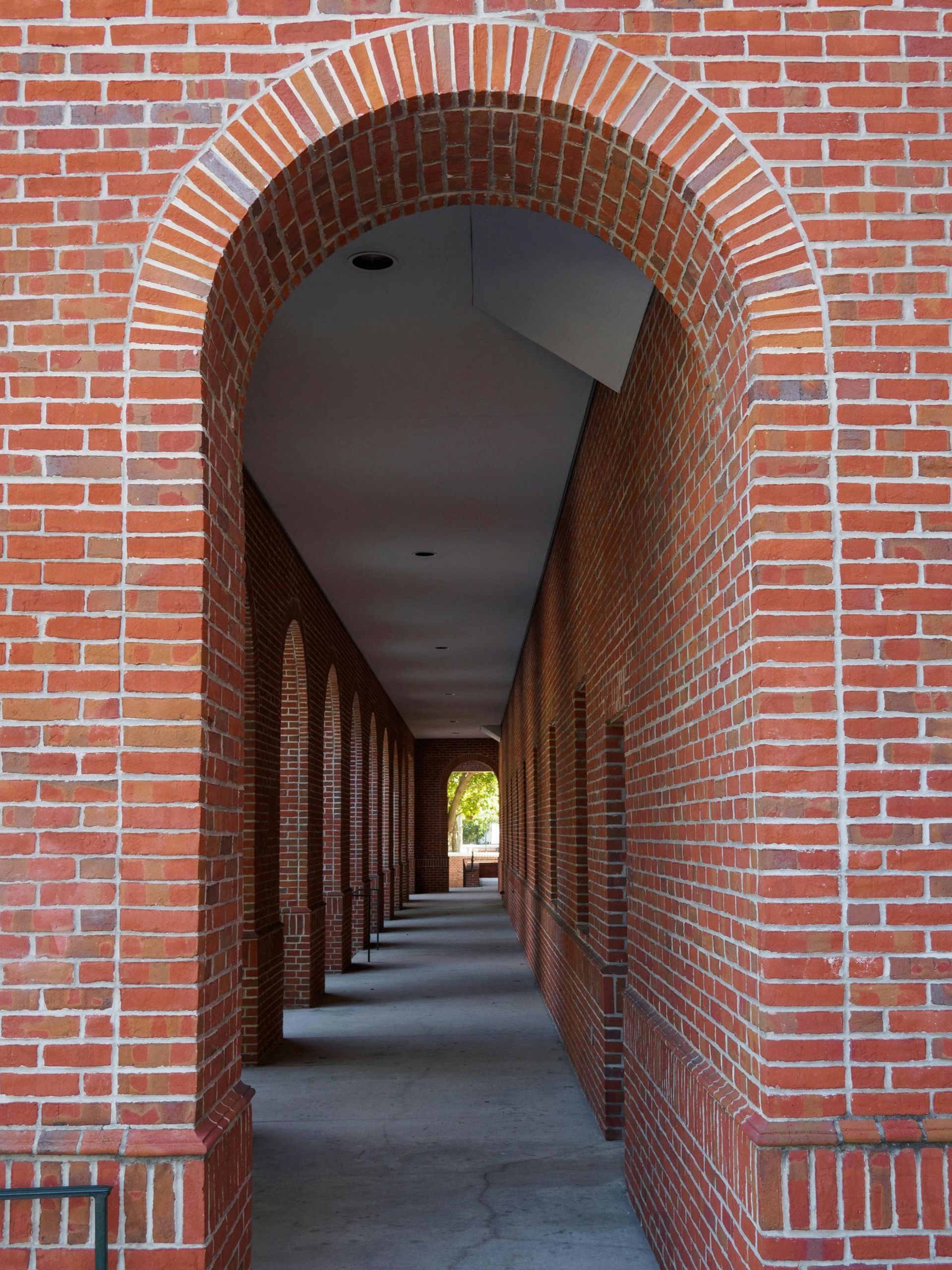 A red brick building featuring a long, arched outdoor corridor leading to a bright exit.