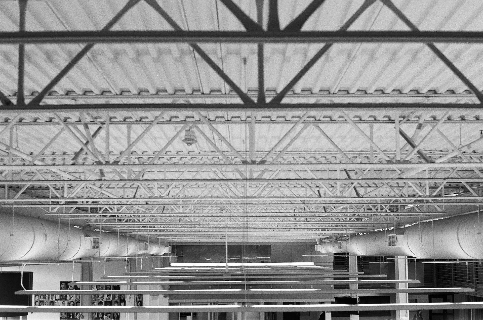 Interior view of a building ceiling featuring white industrial trusses, corrugated metal decking, and suspended HVAC ducts.