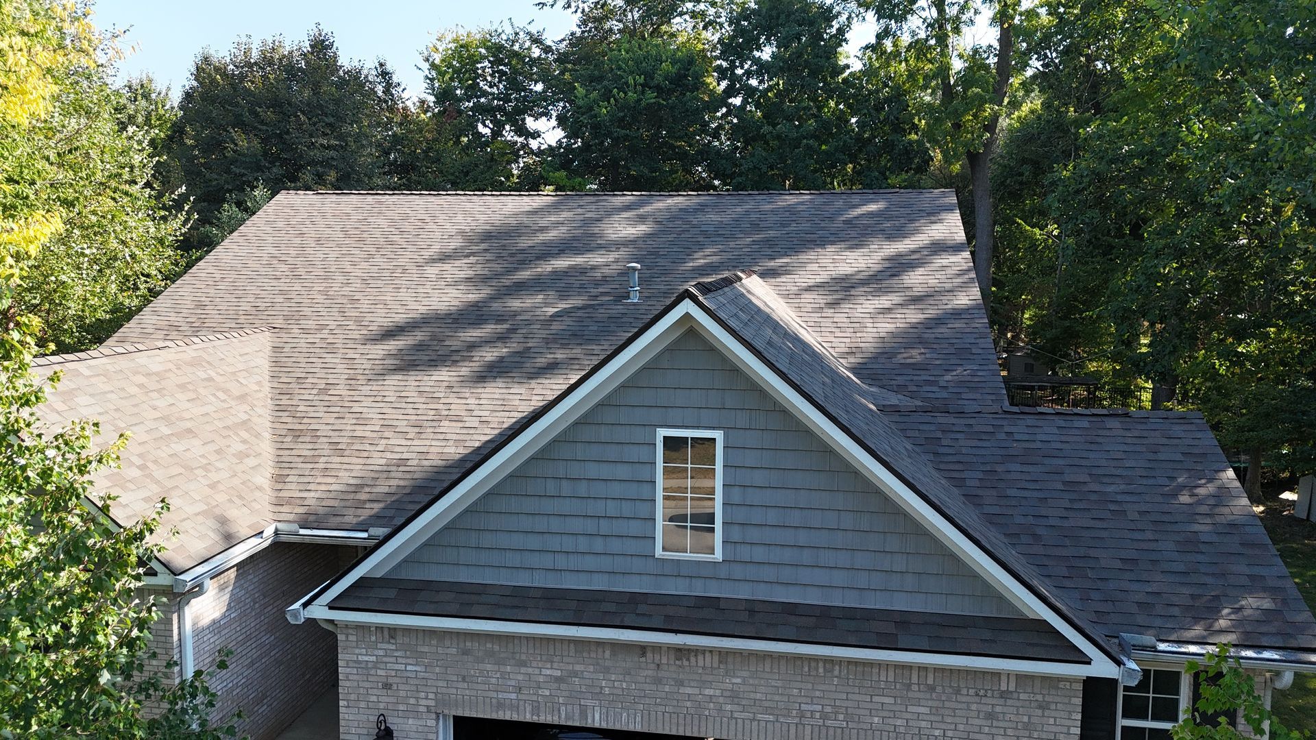 Aerial view of a gray shingled roof on a residential house with a gabled section featuring gray horizontal siding.