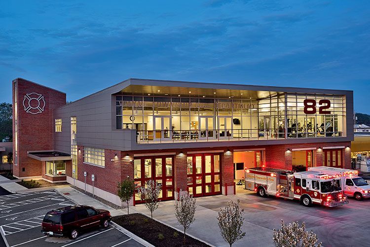 Modern fire station 82 at dusk with a fire engine parked in front and a dark SUV in the lot.