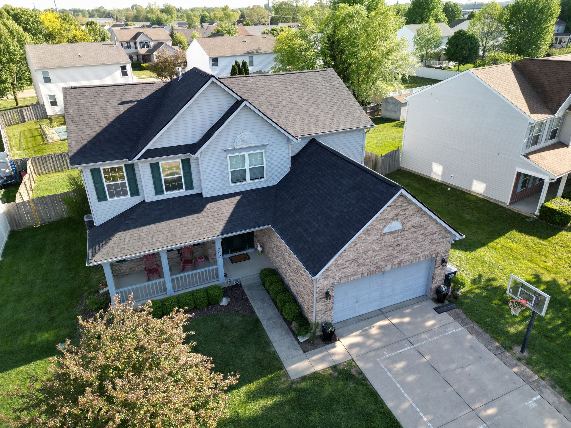 Aerial view of a suburban two-story house with a gray roof, brick facade, and attached garage