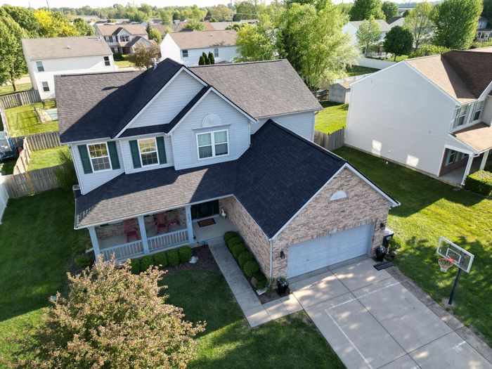 Aerial view of a two-story suburban house with a gray roof, brick facade, driveway, and basketball hoop.