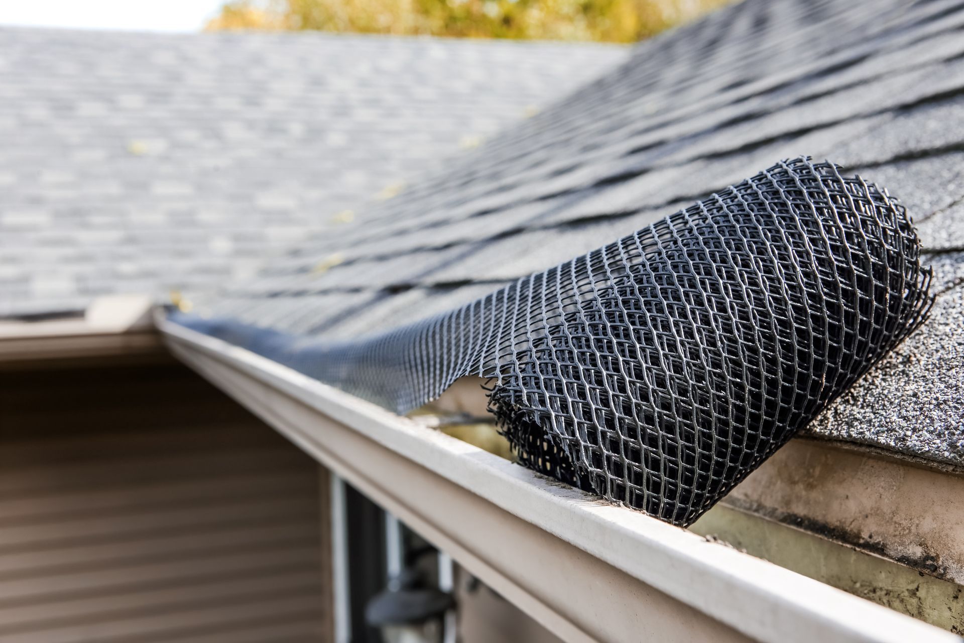 A black, mesh-style gutter guard roll sitting on the edge of a residential roof near the gutter.