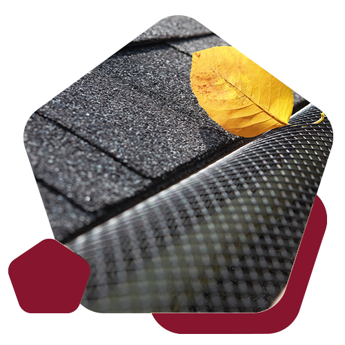 A single yellow leaf resting on a black mesh gutter guard installed below dark asphalt roof shingles.