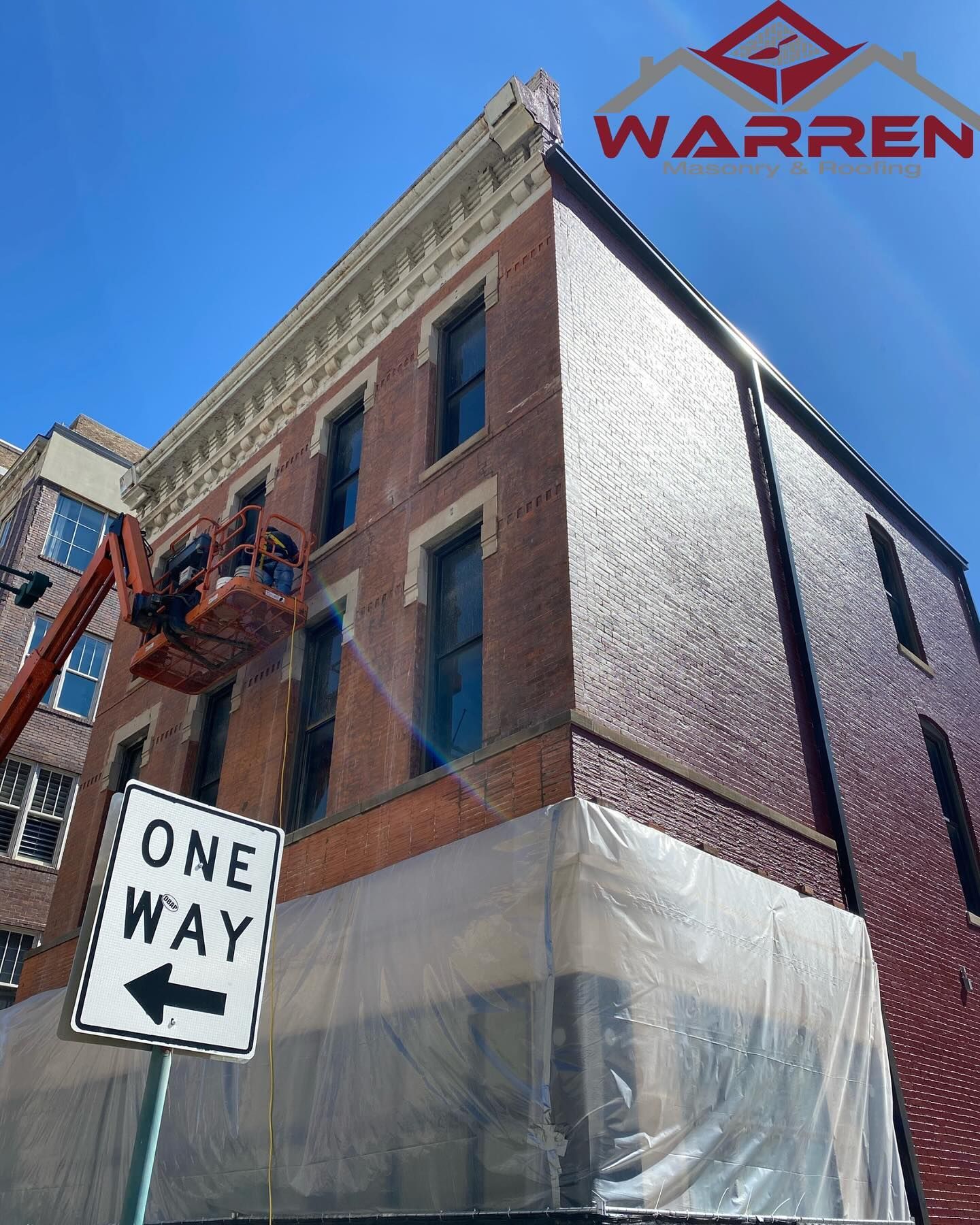 Brick corner building with scaffolding, Warren sign, and one-way street sign against a blue sky
