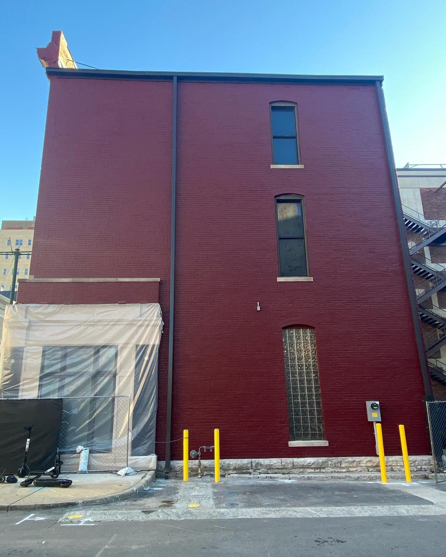 Red brick building facade with tall narrow windows and yellow bollards on a snowy street