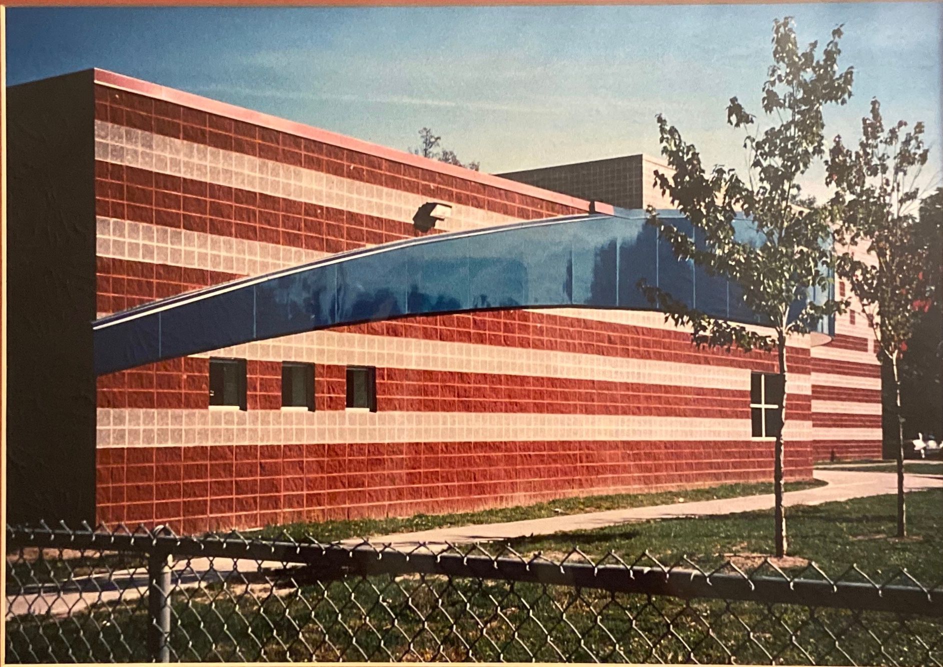 A modern building with horizontal red and white brick stripes, featuring a prominent blue curved awning and small windows.