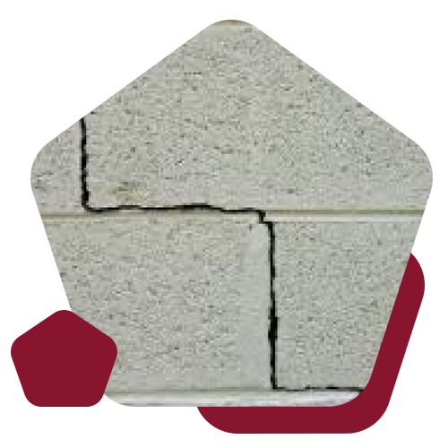 A close-up view of structural cracks forming along the mortar joints of grey concrete masonry blocks.