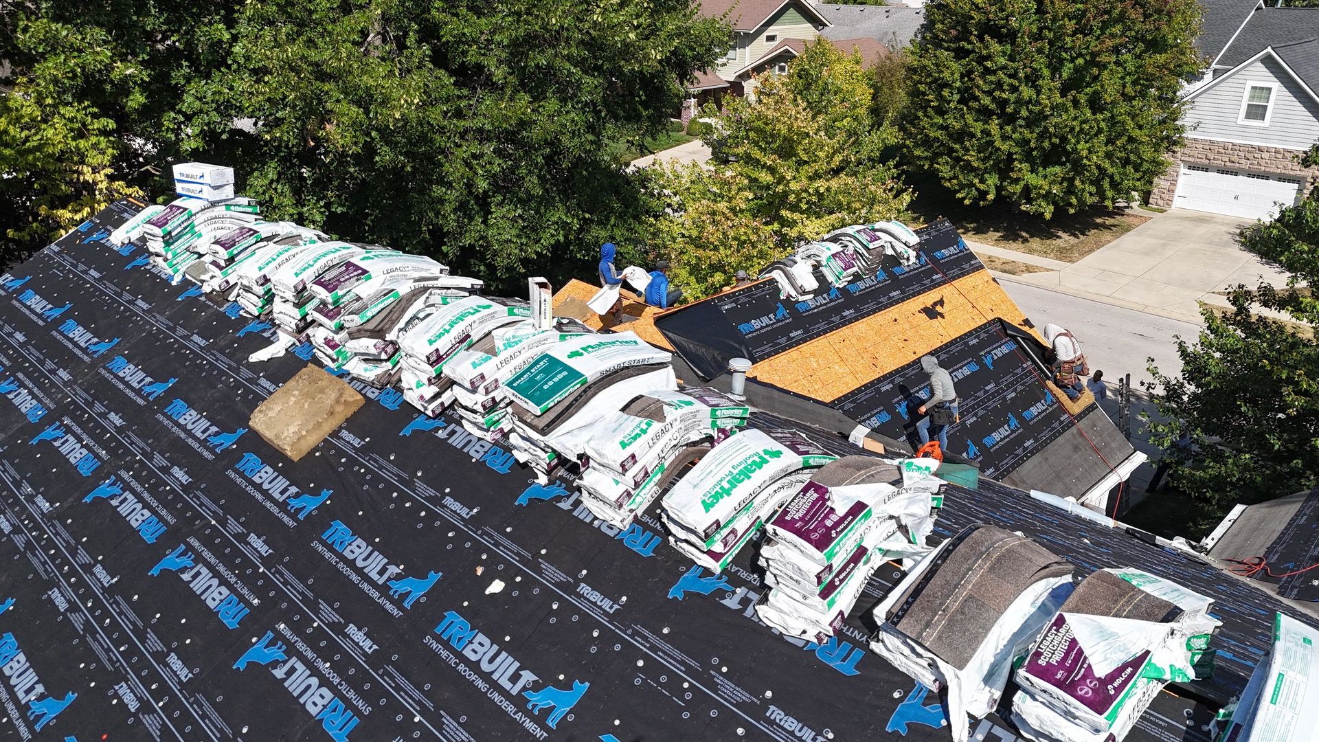 Workers installing new roof shingles on a residential home covered in black underlayment.