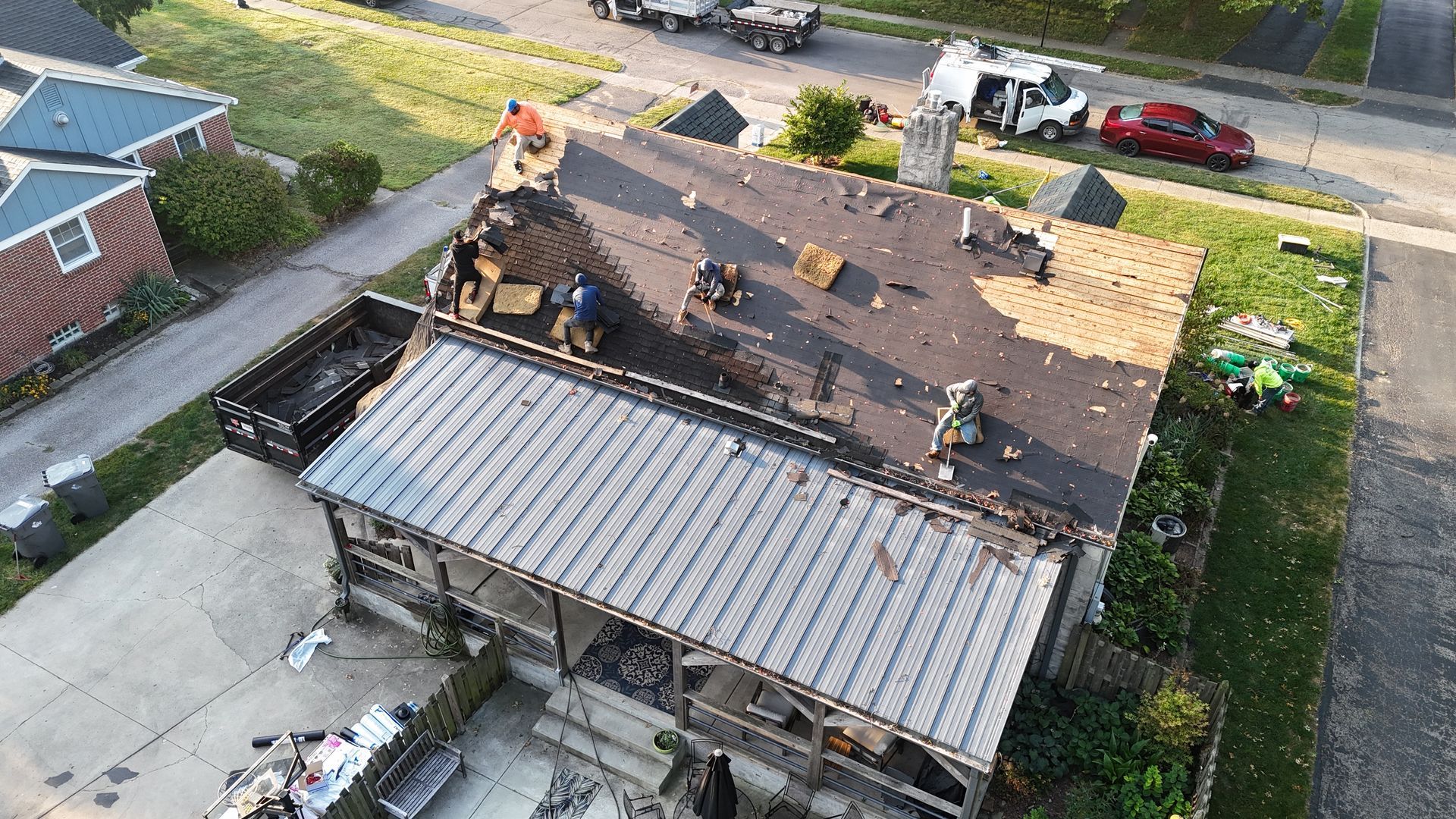 An aerial view of a residential roof replacement in progress, with workers removing shingles and exposing the deck.