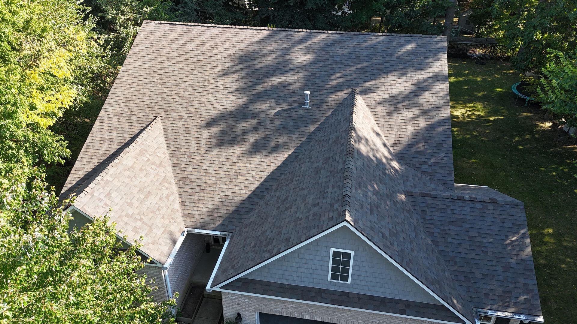 An aerial view of a gray-shingled roof on a residential house surrounded by green trees in Indianapolis.