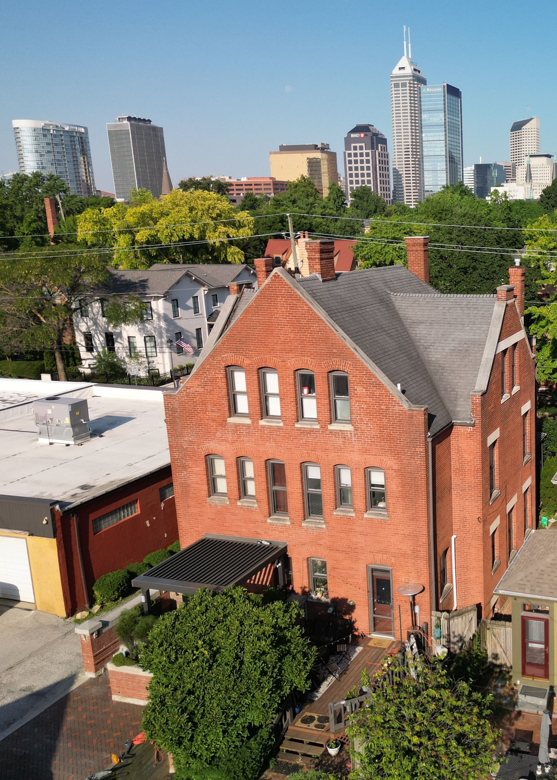 Red brick house with steep roof in a city neighborhood, with modern high-rises in the background.