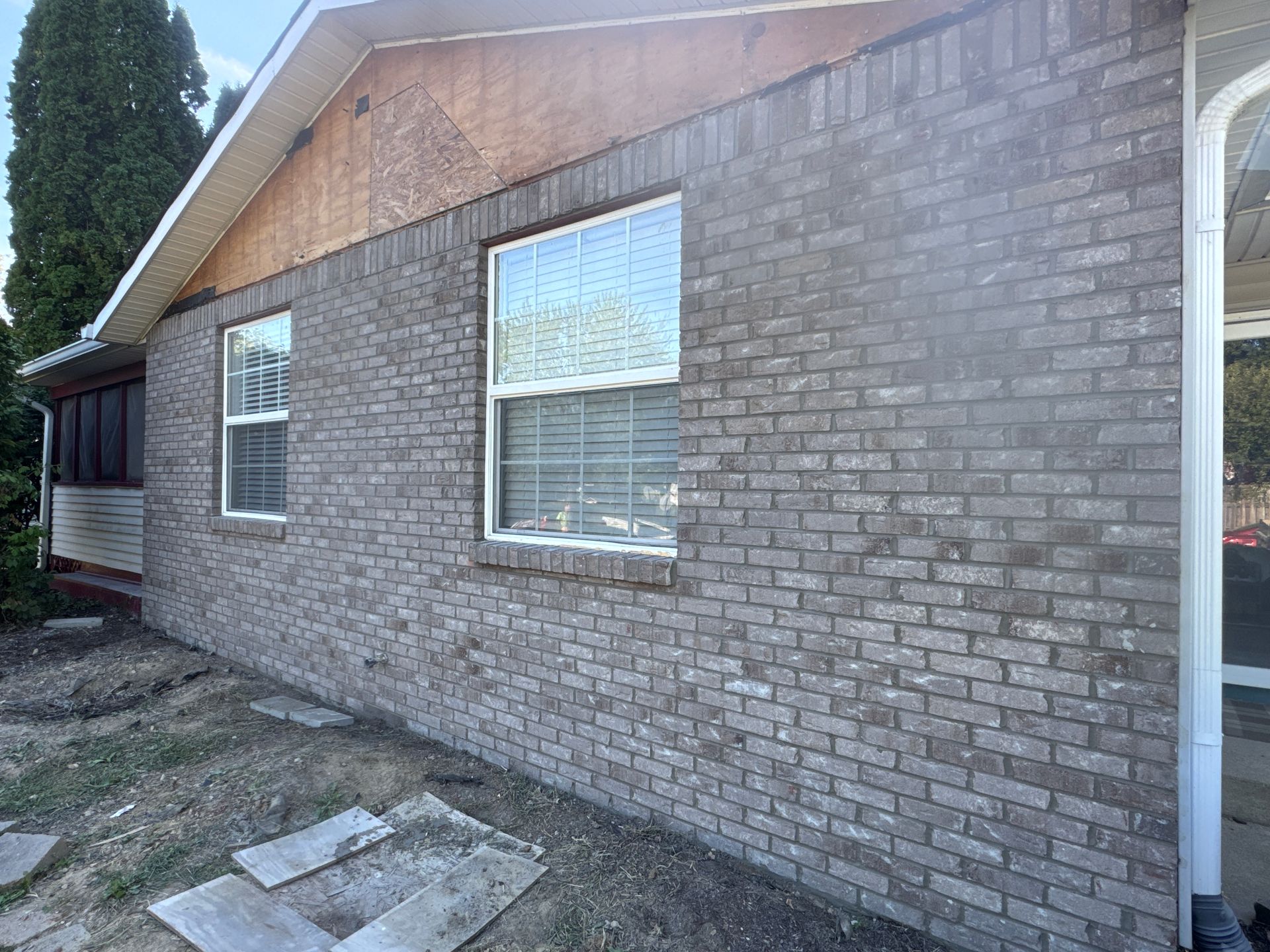 Side view of a brick house exterior with two windows and a small concrete patio area
