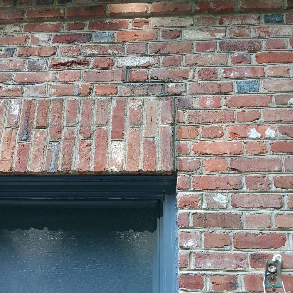 A close-up view of a red brick wall featuring a vertical soldier course header above a dark-framed doorway.