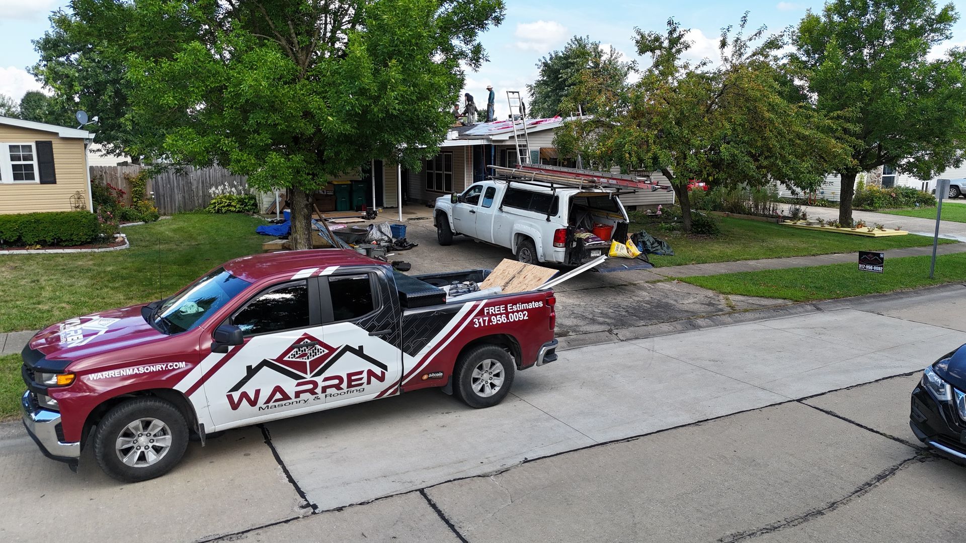 A Warren roofing company pickup truck parked on a residential street in front of a house undergoing roof work.