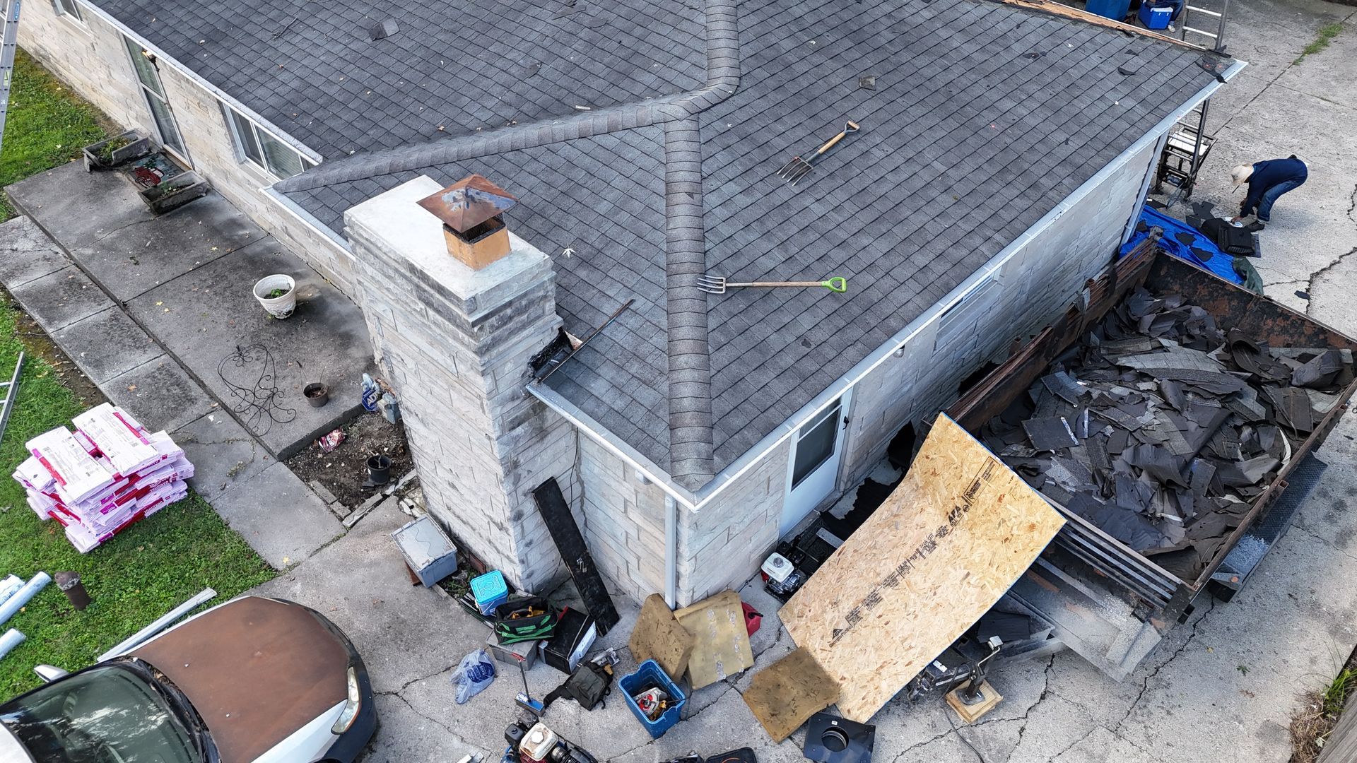 An aerial view of a house undergoing a roof replacement, featuring materials, equipment, and a dumpster filled with debris.