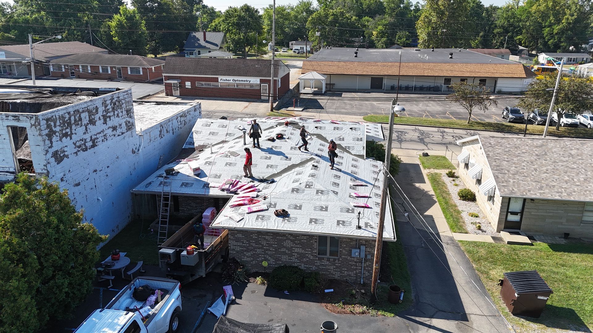 An aerial view of construction workers installing new underlayment on the roof of a commercial building.