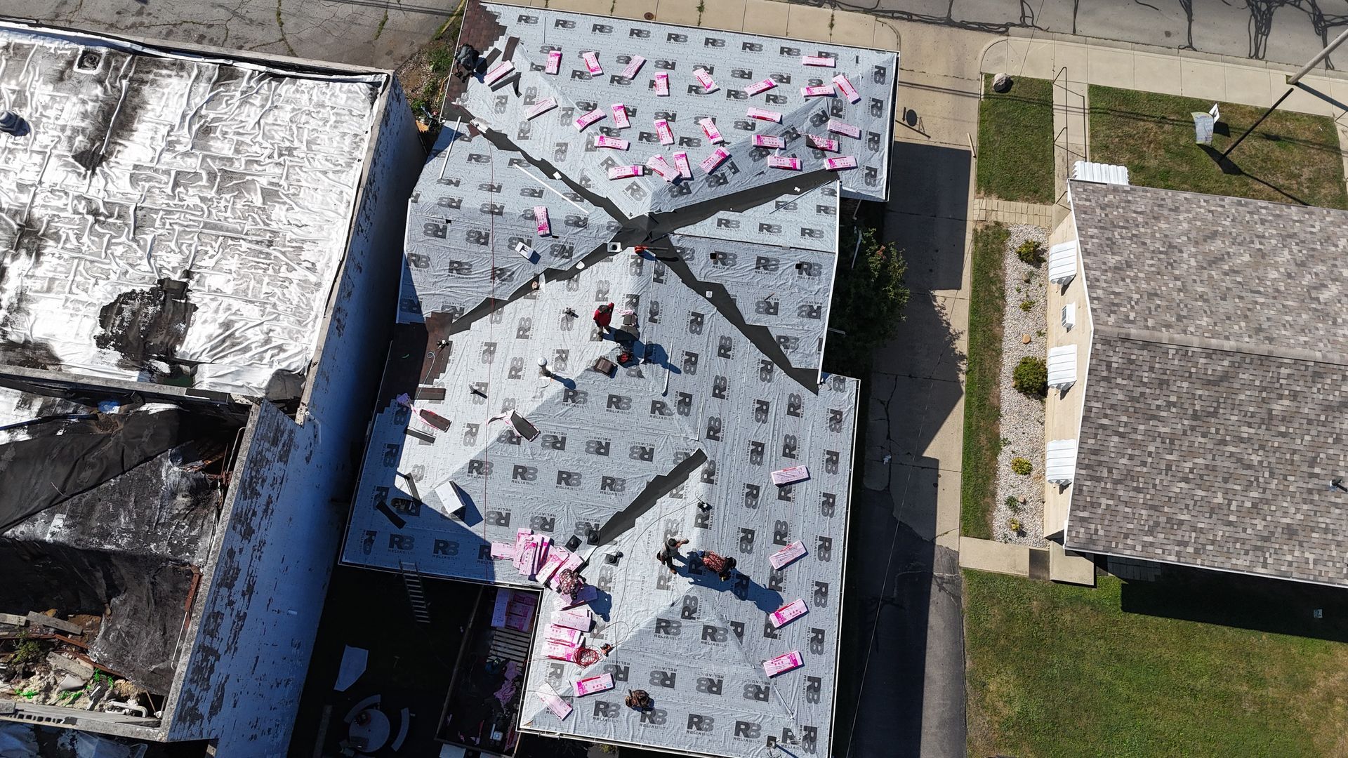 Aerial view of workers installing light-colored roofing underlayment on a residential roof.