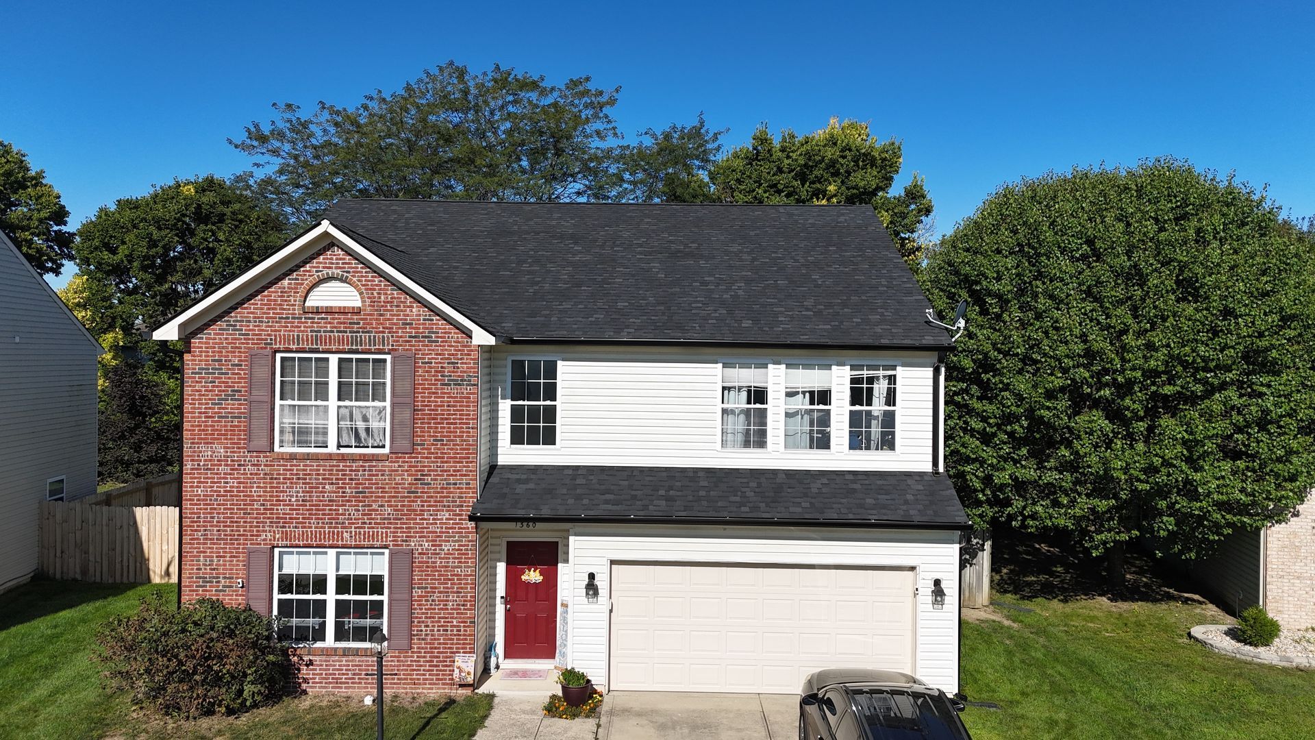 A two-story house with a brick left side, white siding on the right, a dark roof, and a red front door under a blue sky.