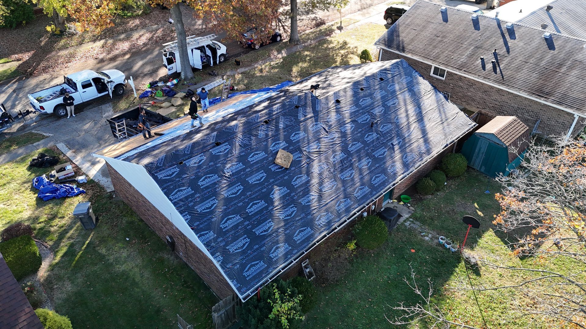 An aerial view shows workers installing dark synthetic underlayment on a residential roof during a renovation project.