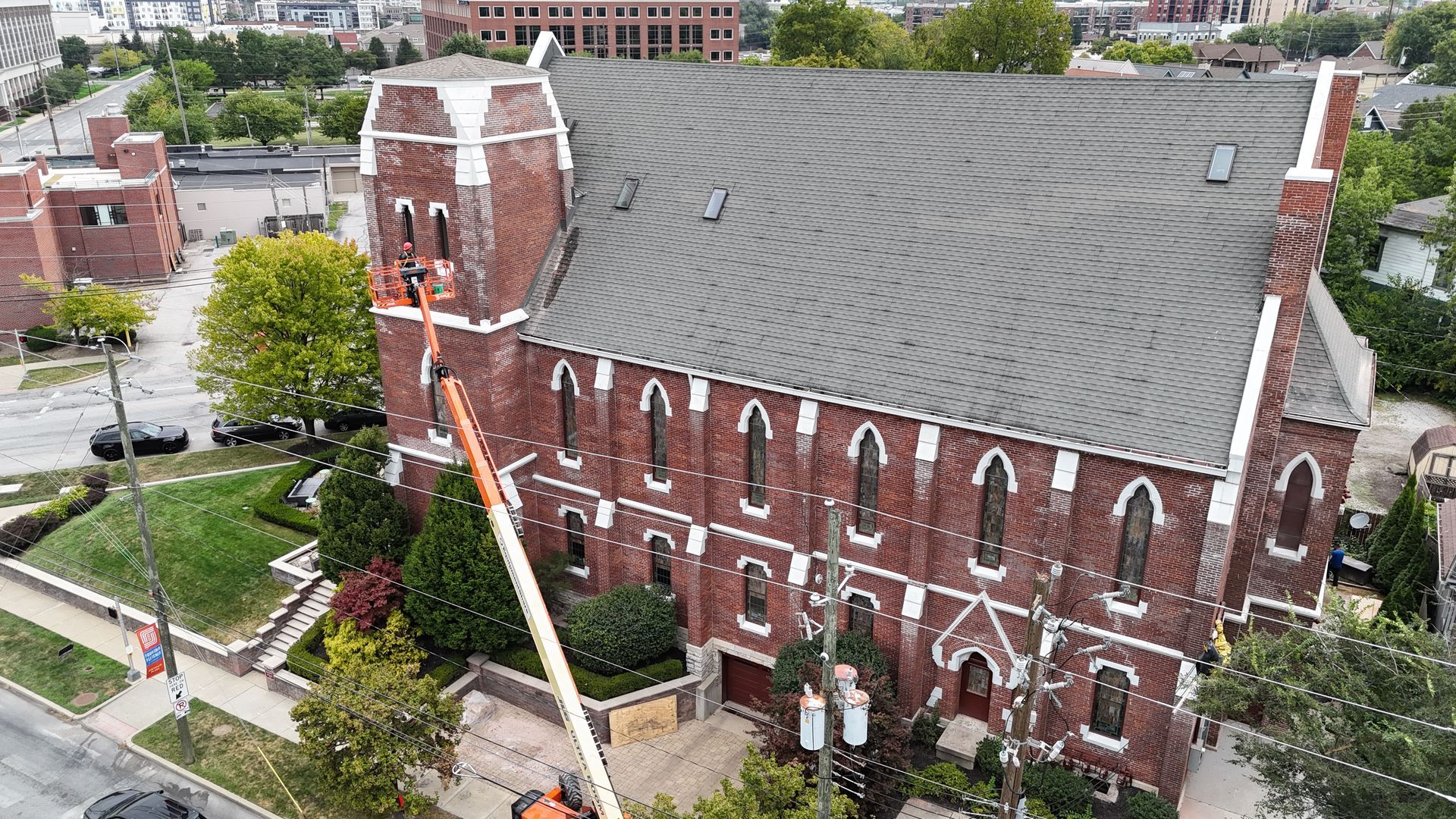 An aerial view of a red brick church with a grey roof, with a crane lift working on the building's facade.