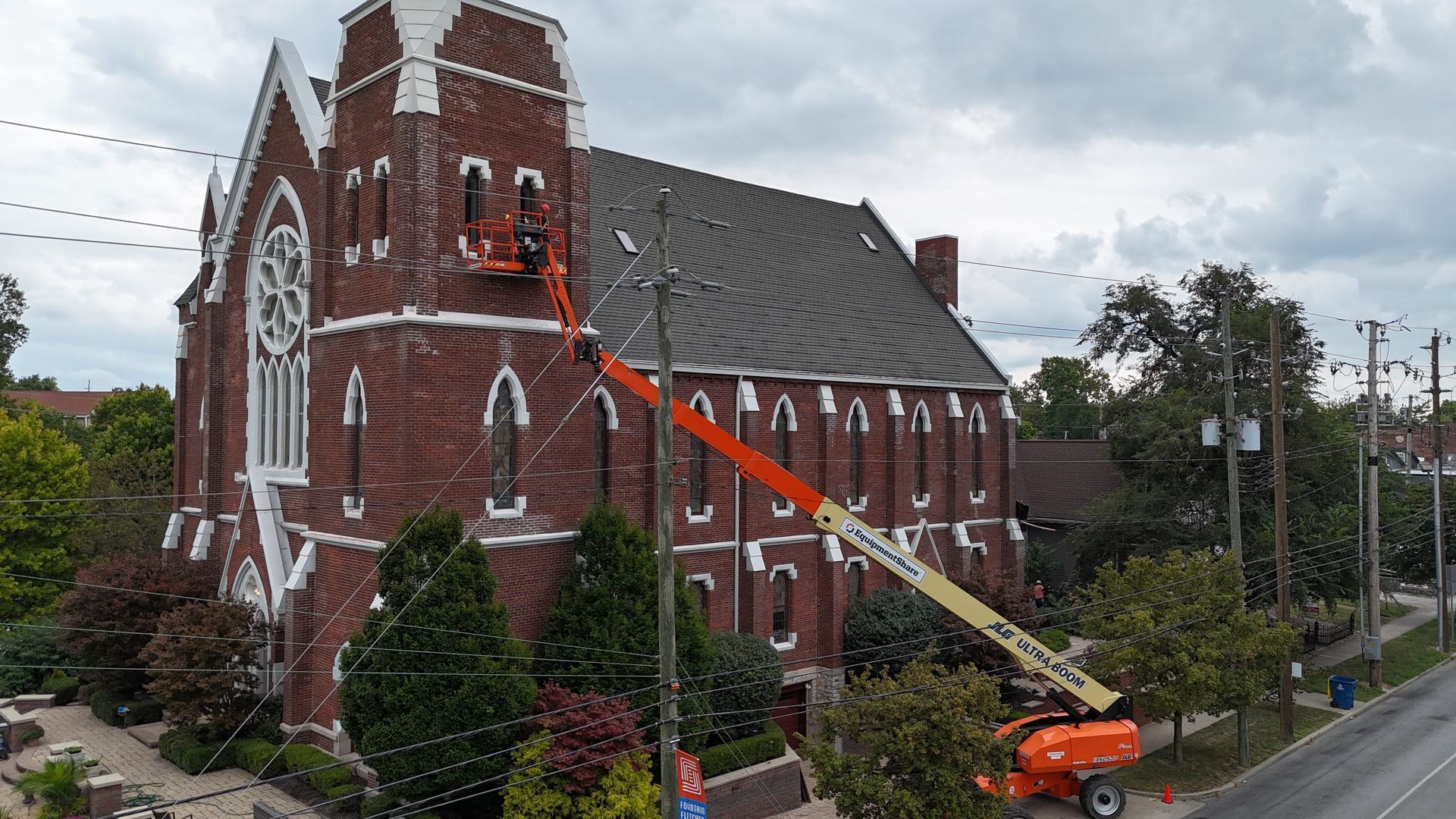 A construction boom lift extends to reach the upper level of a red brick church for maintenance.