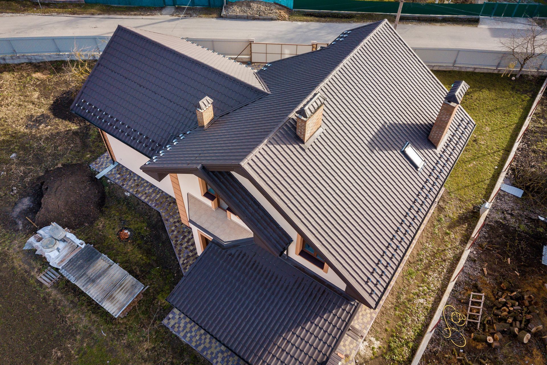 Aerial view of a residential house featuring a complex dark brown metal roof with chimneys and a small skylight.