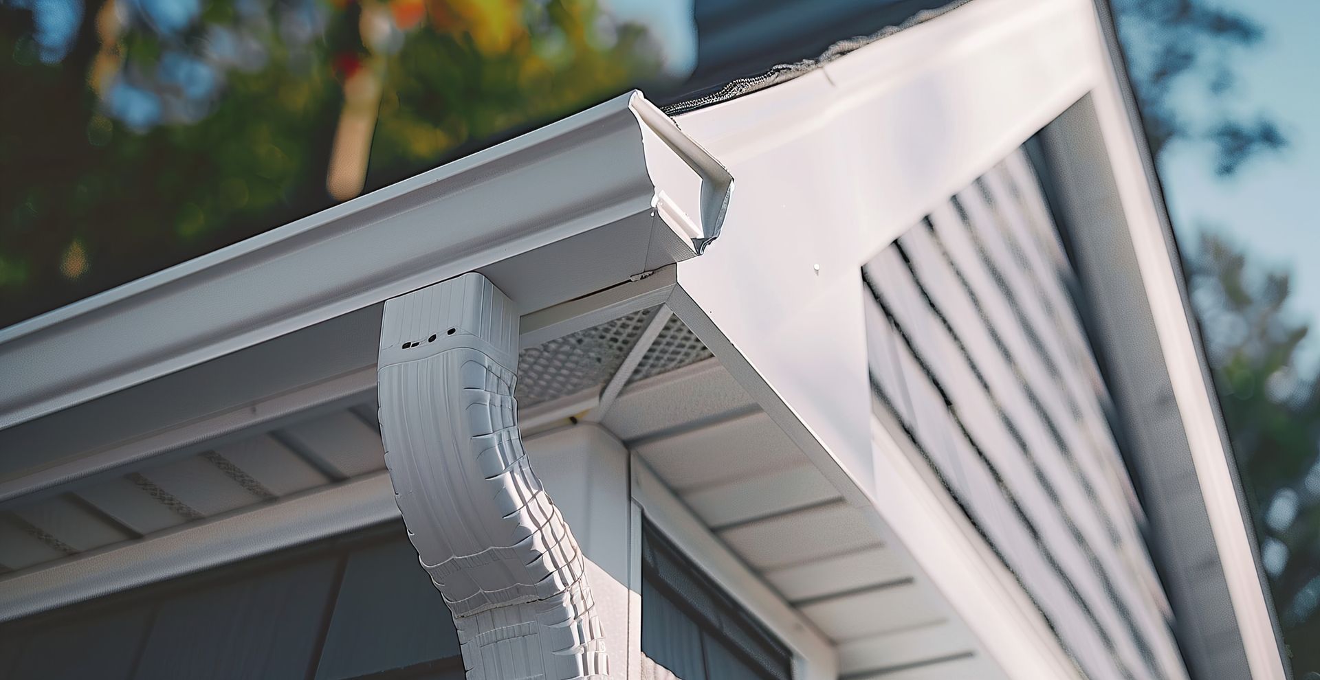 White house corner featuring a clean, white metal gutter system and downspout against a dark brown exterior wall.