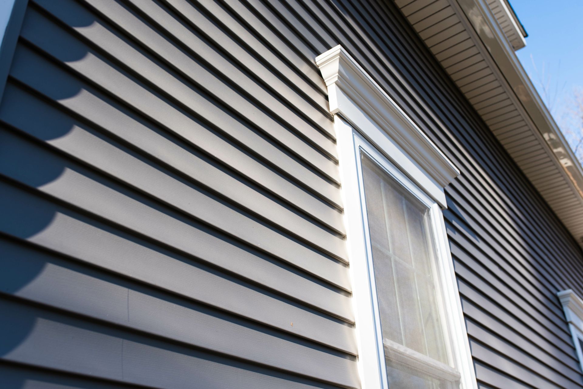 A close-up view of dark grey horizontal vinyl siding on the exterior wall of a house, featuring a white-trimmed window.