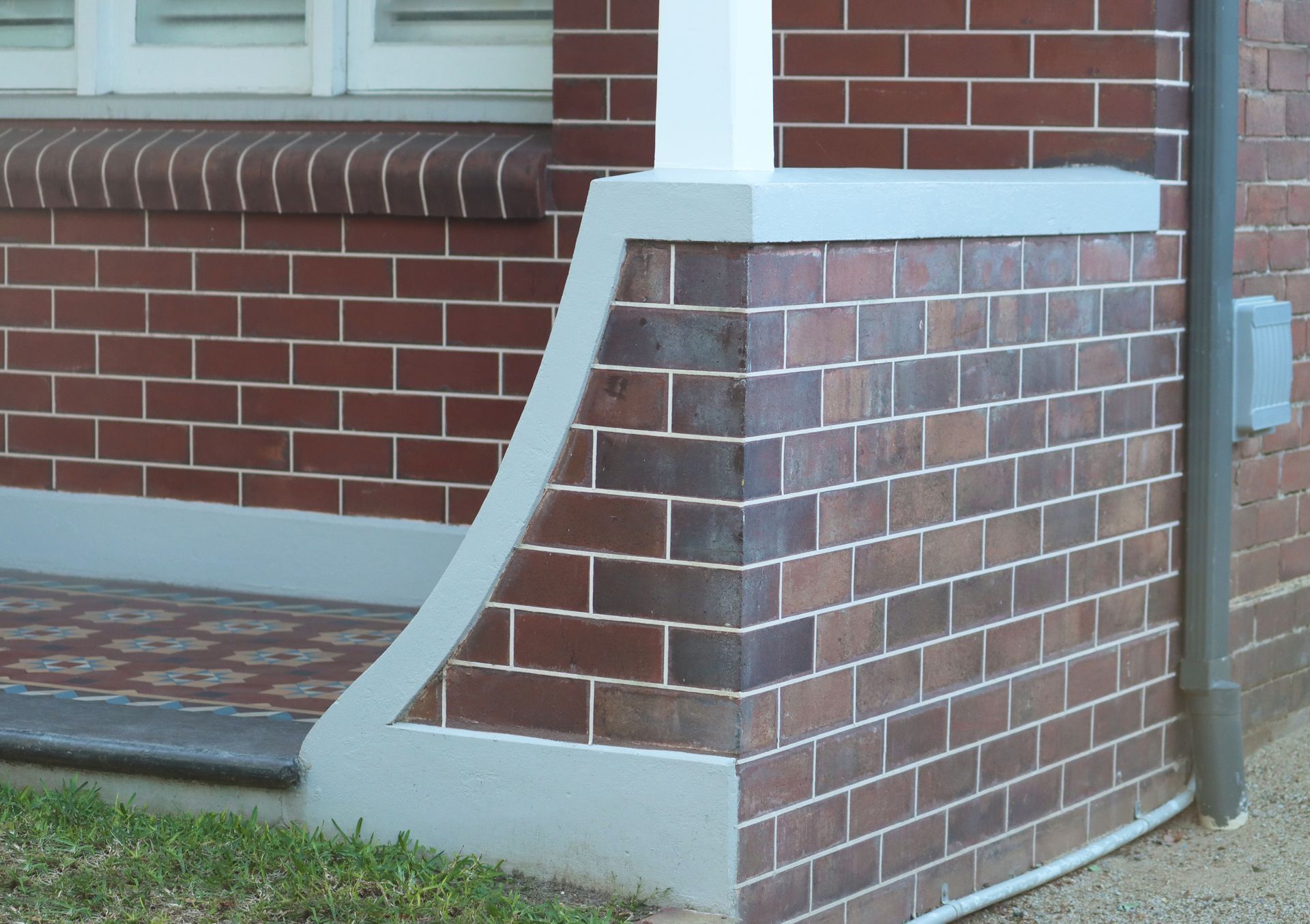 A close-up of a brick building exterior, featuring a white-painted masonry corner pillar on a patio with tiled flooring.